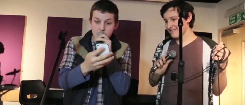 Two young people recording vocals with microphones in the studio
