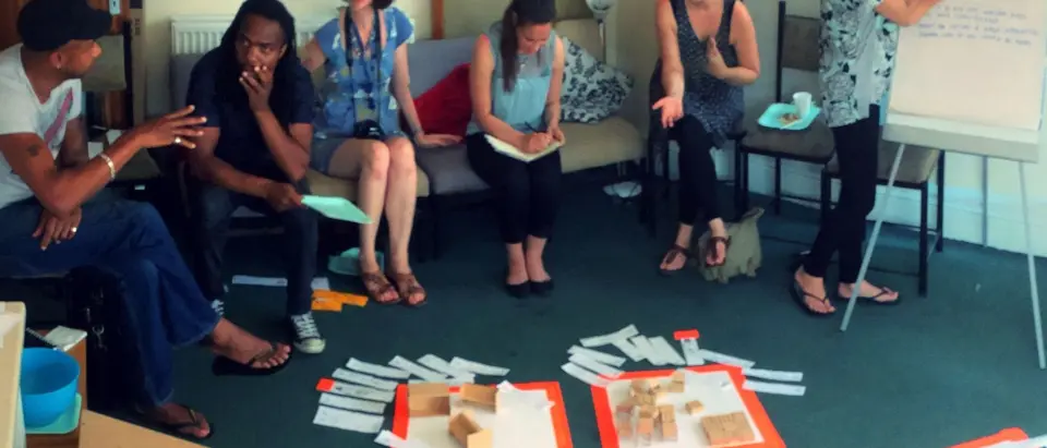 A group sitting in a circle during a SEND Project workshop, with craft materials laid out on the floor