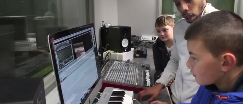 A young person learning music production on a computer and keyboard with a SEND tutor
