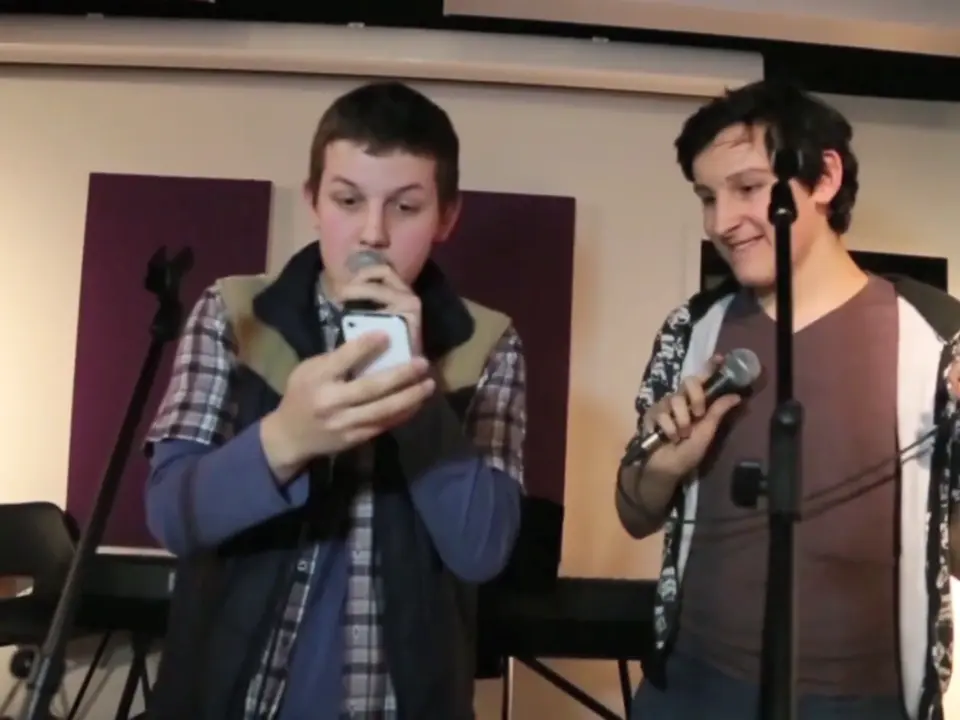 Two young people recording vocals with microphones in the studio