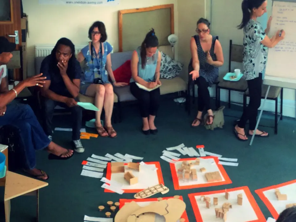 A group sitting in a circle during a SEND Project workshop, with craft materials laid out on the floor