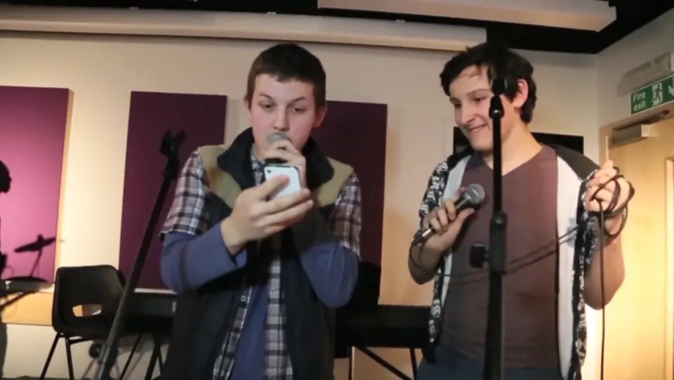 Two young people recording vocals with microphones in the studio