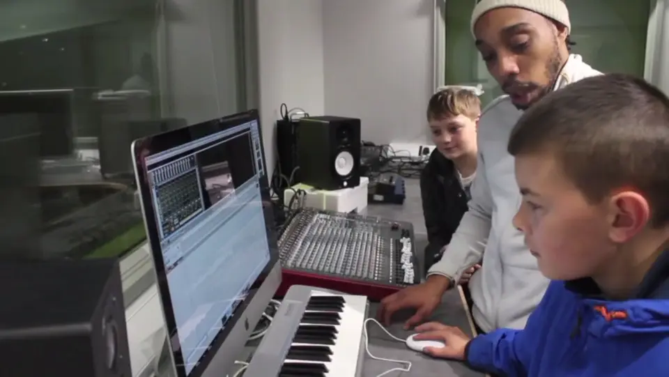 A young person learning music production on a computer and keyboard with a SEND tutor