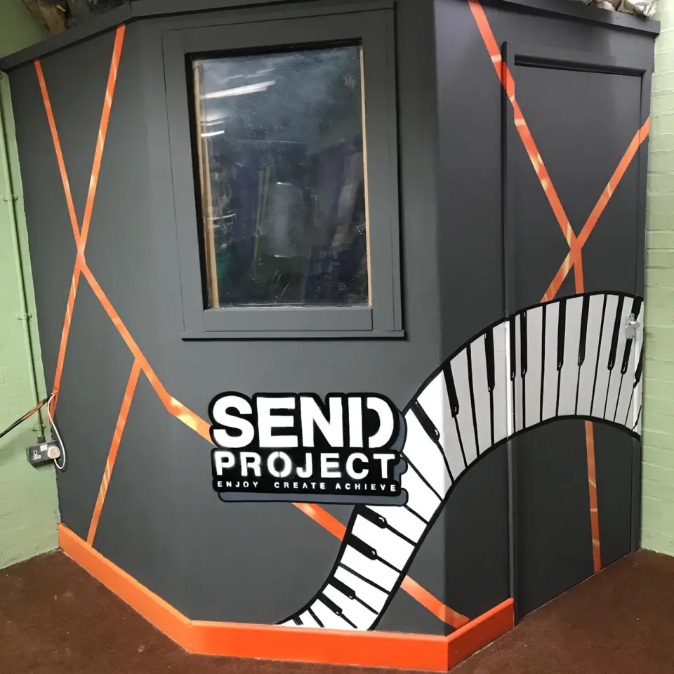 The SEND Project recording booth, painted with an orange outline and a piano-key mural